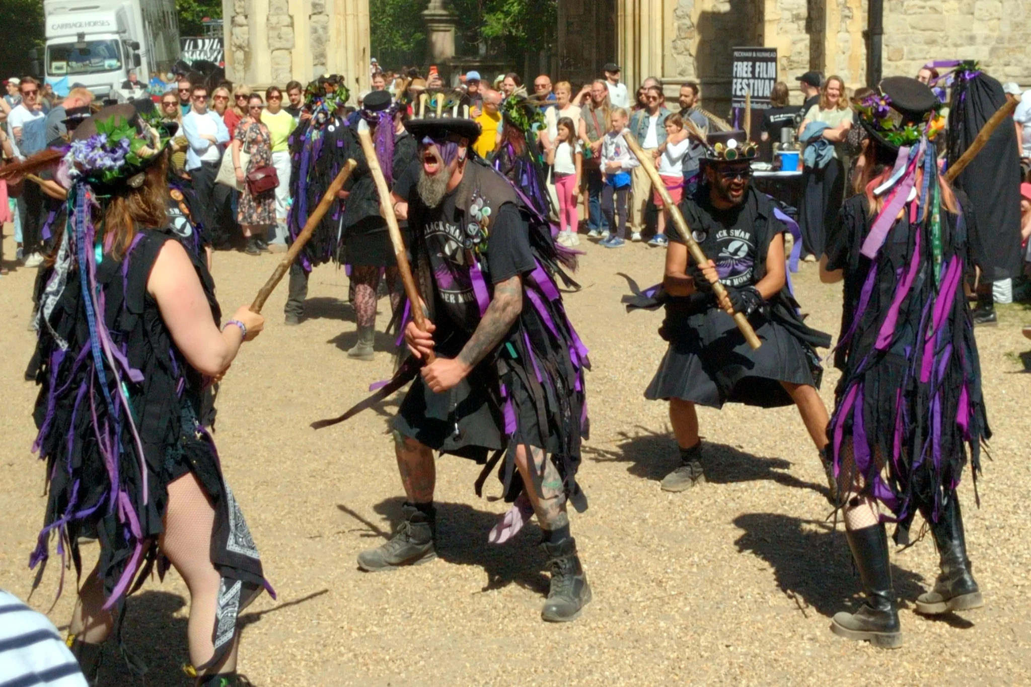 Morris dancers. They are dressed in black with purple accents, and are
striking their sticks with each other and shouting.