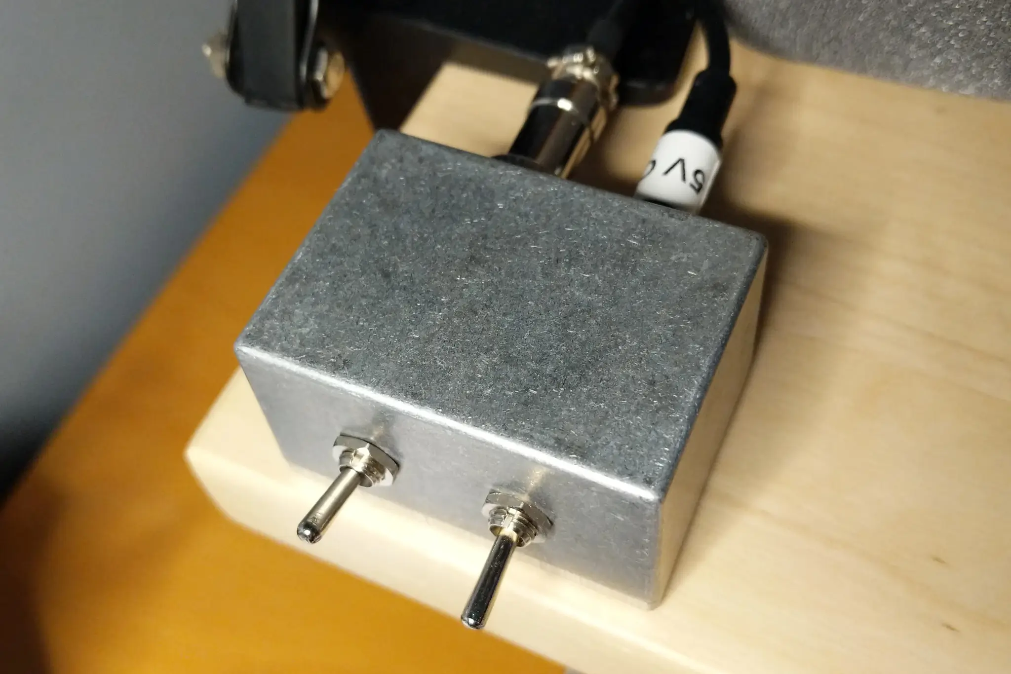 A small aluminium box, about 5 cm across, with two metal toggle switches
on the front and two cables connected at the rear.