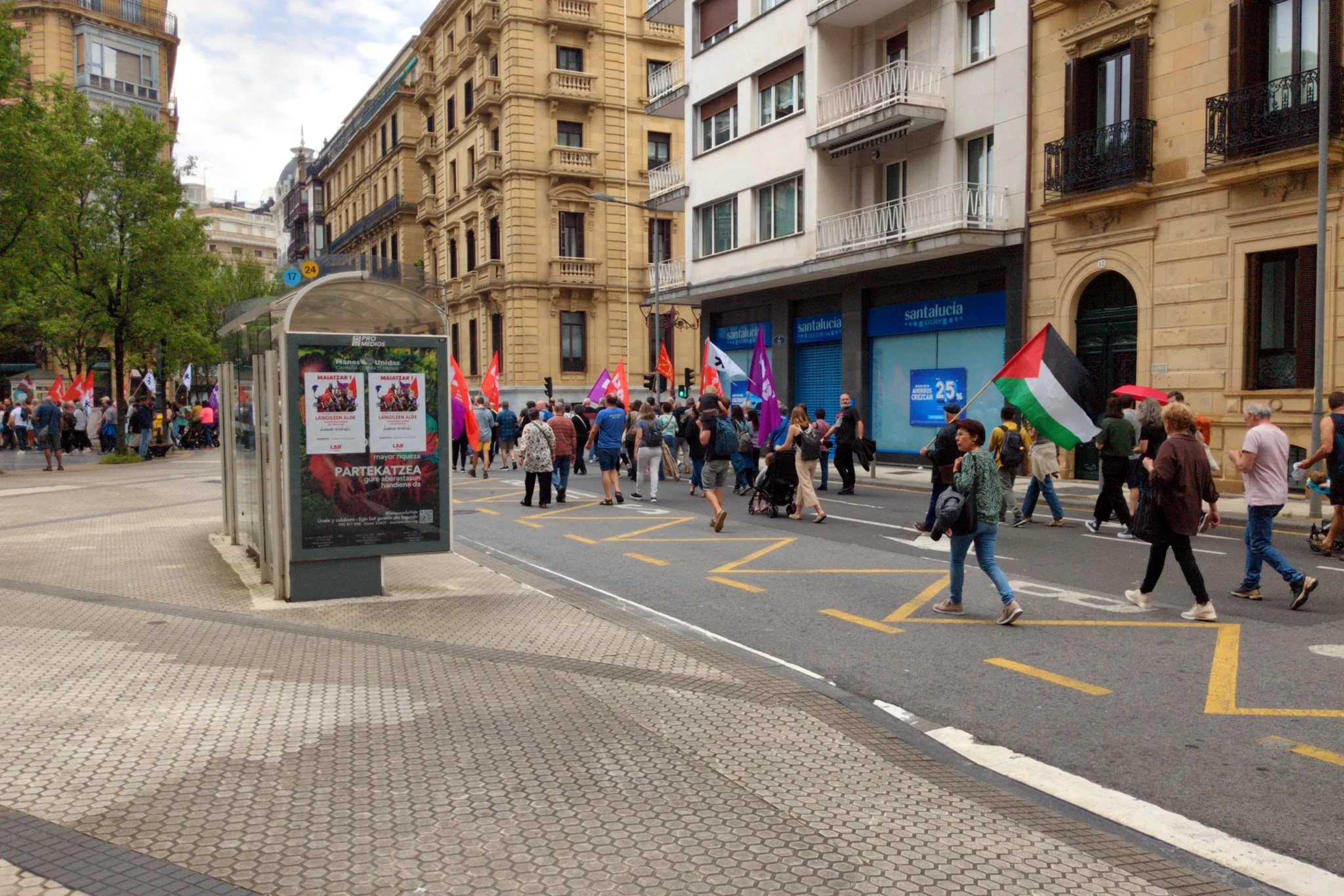 People marching. There are red banners and a Palestinian flag. Posters
on a bus stop advertise the march in Basque.