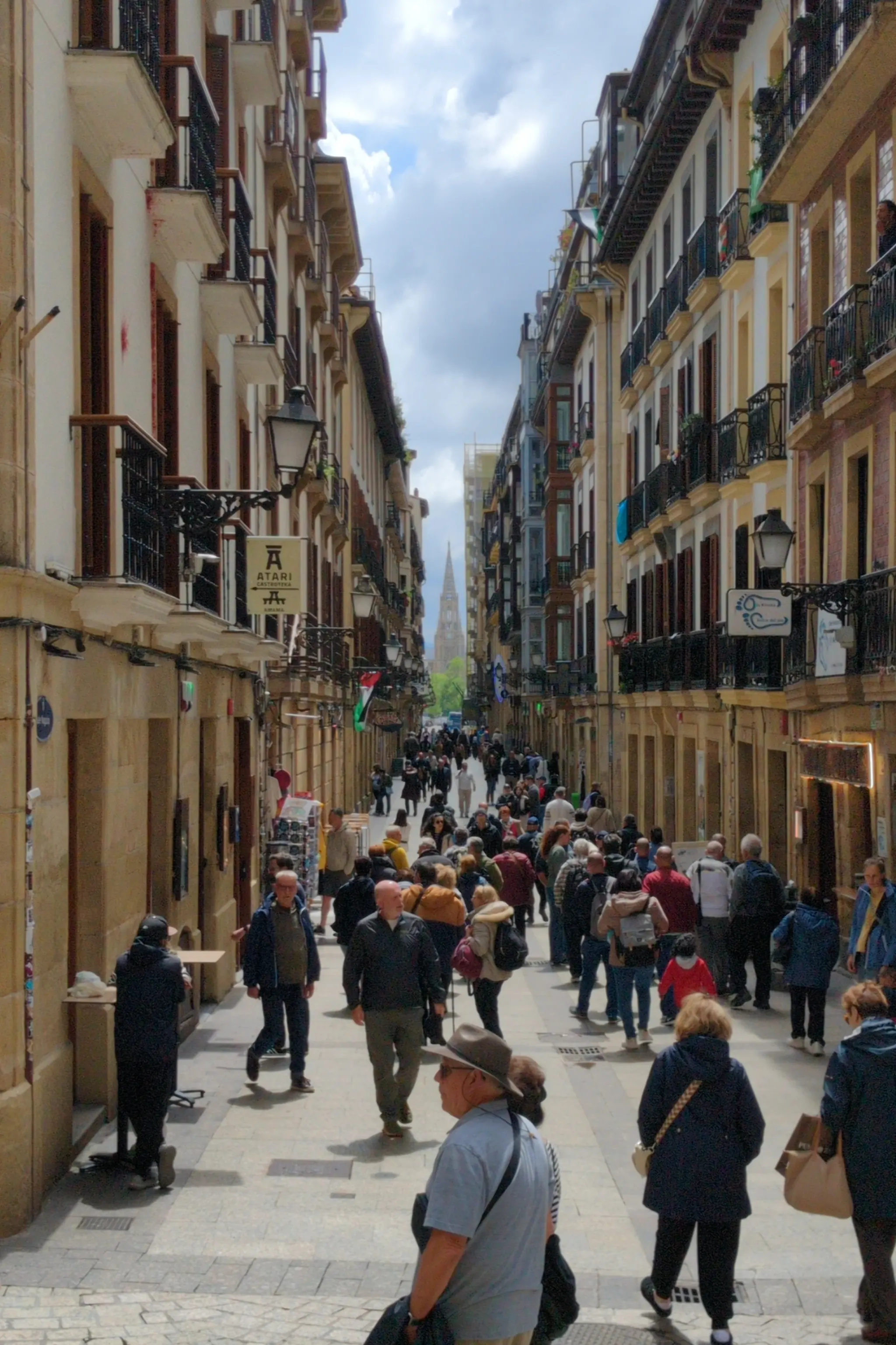 A view down a street full of tourists. There is a cathedral with a spire
in the distance at the end of the street.