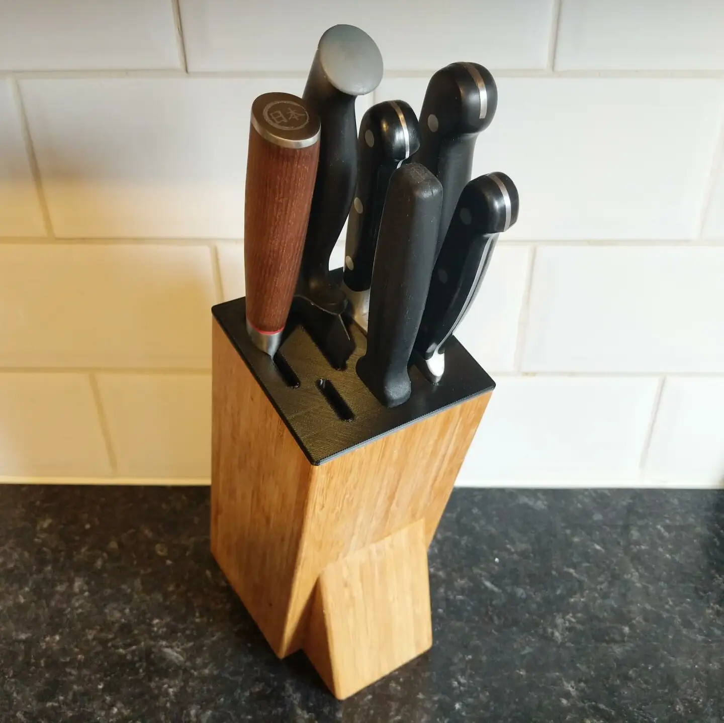A bamboo block with a black 3D printed plastic insert in the top. It has a
variety of long and short slots into which knives are inserted