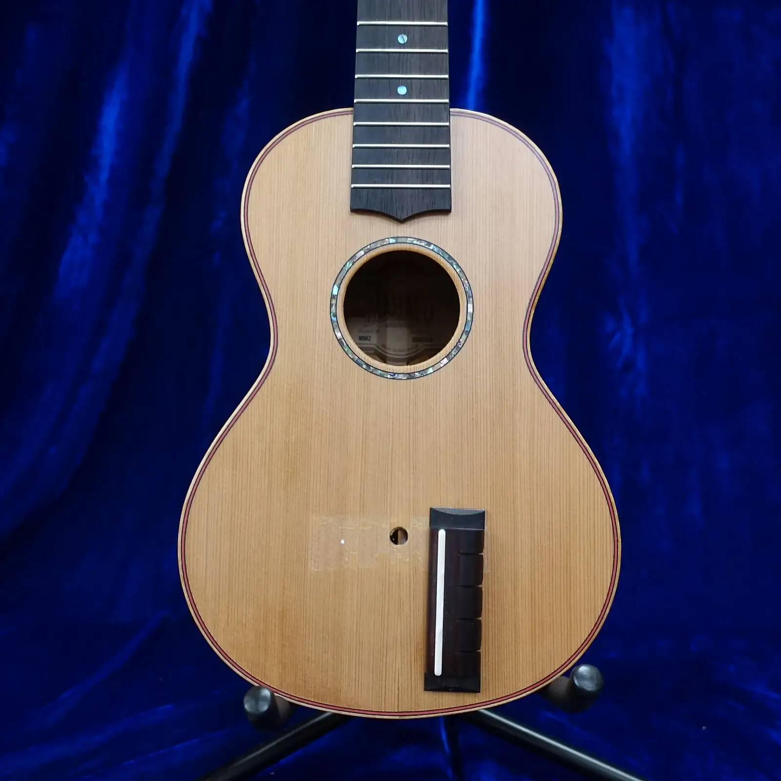 The lower part of a concert ukulele. It has some elaborate construction
details like inlaid purfling around the edge in contrasting colours. However,
the bridge is hanging off, turned through ninety degrees, and it's clear that
the bridge was glued on top of the varnish, some of which has been pulled away.