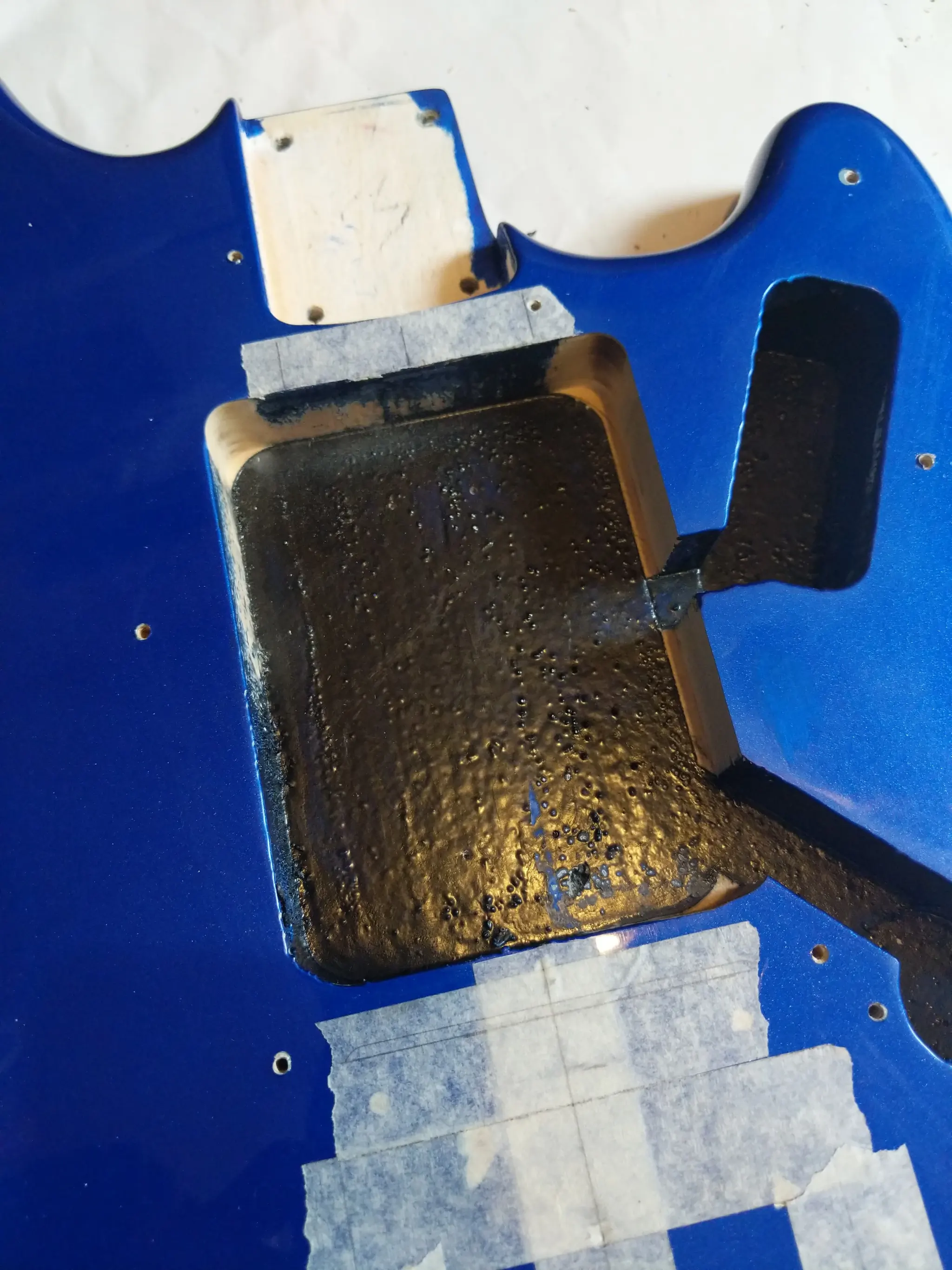 The inside of a guitar beneath the pickguard. There is a large central
cavity, painted black except there the edges have been enlarged by routing.