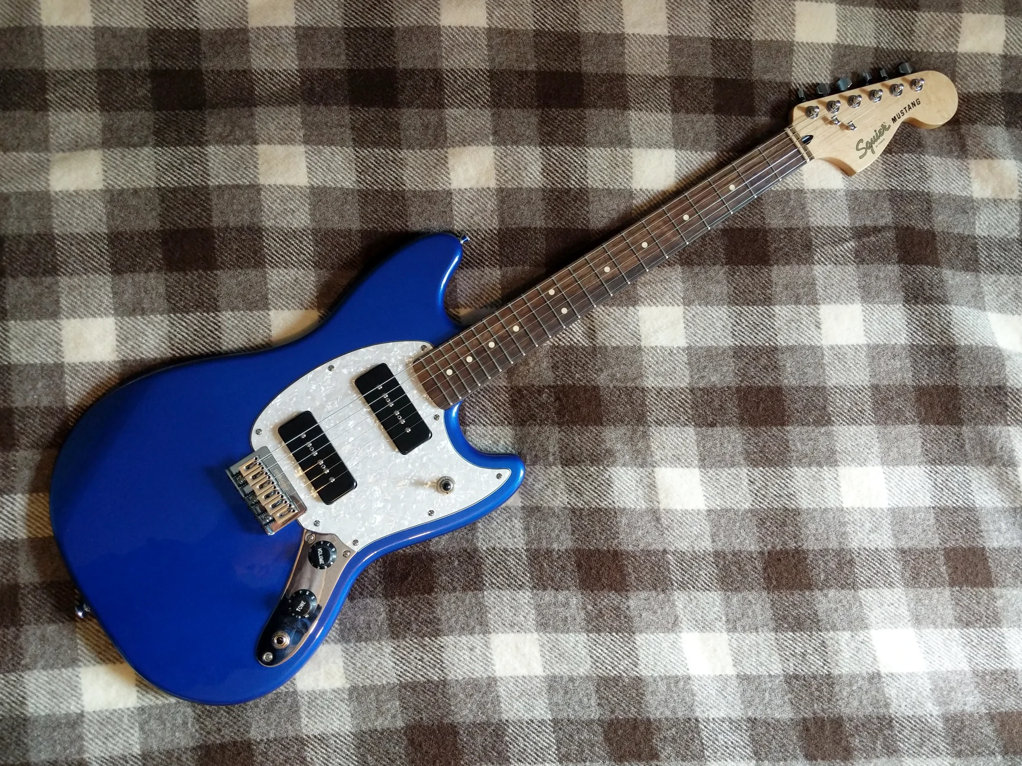 A Squier Mustang guitar on a blanket. It has P-90 pickups and a
pearlescent pickguard