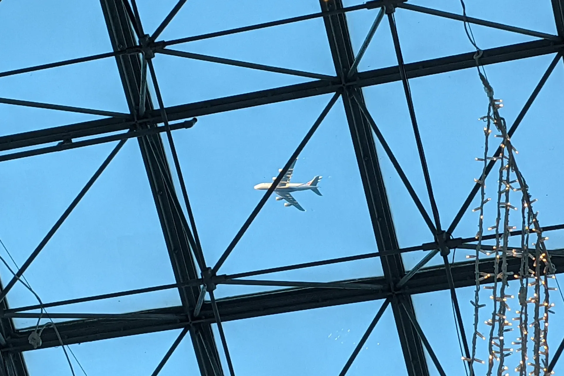 A plane flies directly above, at low altitude, seen through a skylight
window of Surrey Quays Shopping Centre.