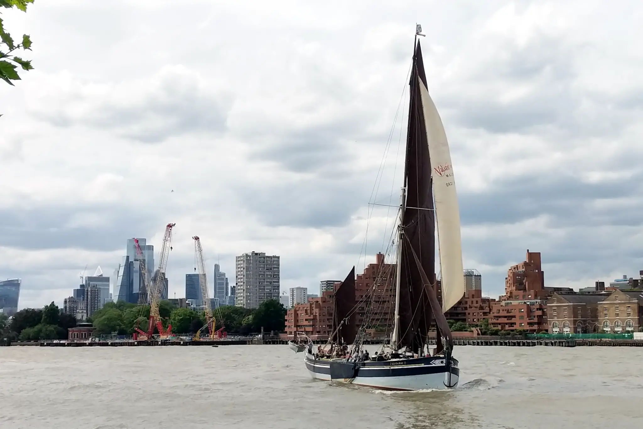 A barge sailing on the Thames. In the background the towers of the City of
London are visible, as are the cranes of the super sewer site at Wapping. The
tide is high