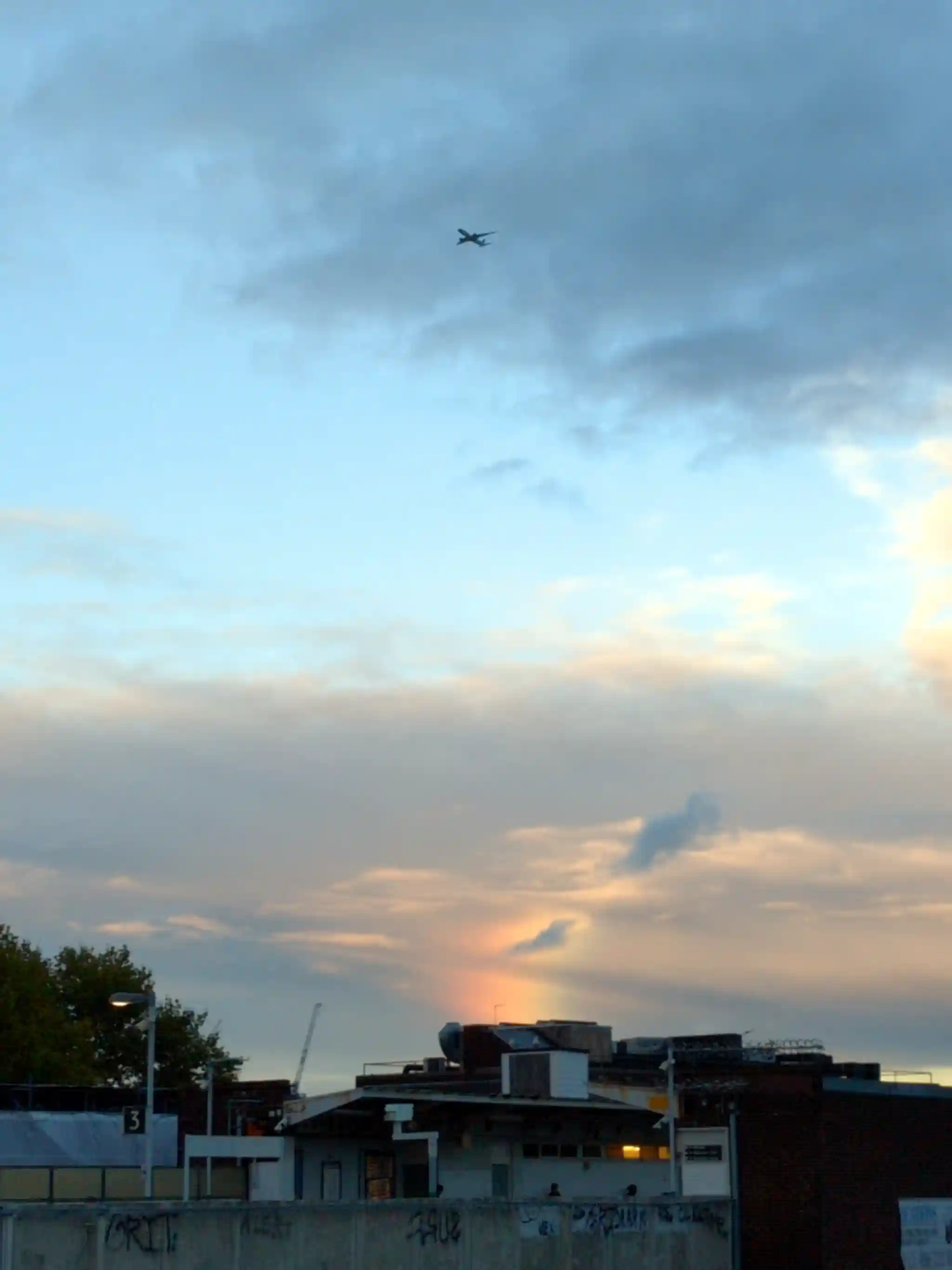 Dark clouds, a partial rainbow, blue skies above, and an aeroplane up
high, taken from a railway platform