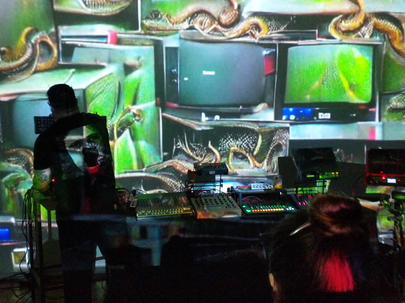 Iggor Cavalera
bends over a table full of synthesisers. A GAN-generated image of an impossible
scene that seems to be old TVs and snakes is projected onto the wall.