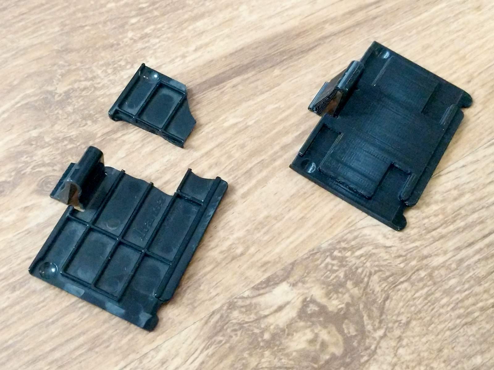 An original broken battery door next to a 3D printed replacement. Apart from a few changes to make it easier to print, they're more or less identical.